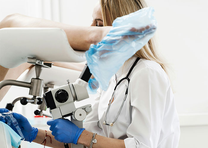 Doctor examining patient wearing blue gloves and plastic foot covers during a medical appointment in a clinical setting