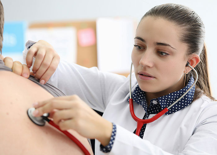 Female doctor using stethoscope during a hilariously embarrassing doctor’s appointment with a patient in a clinic.