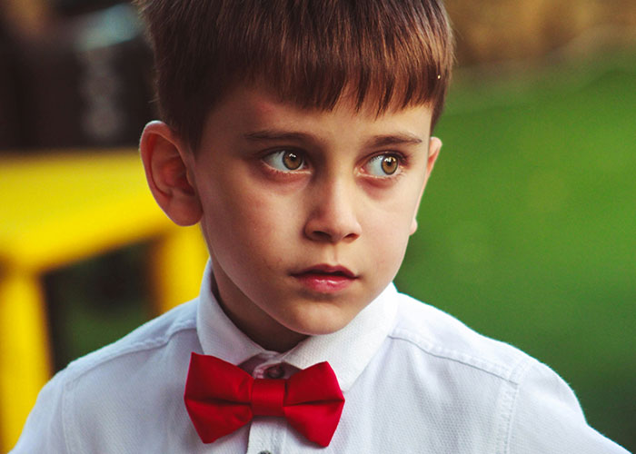 Young boy wearing a red bow tie looking to the side, capturing a moment from a hilariously embarrassing doctor’s appointment.