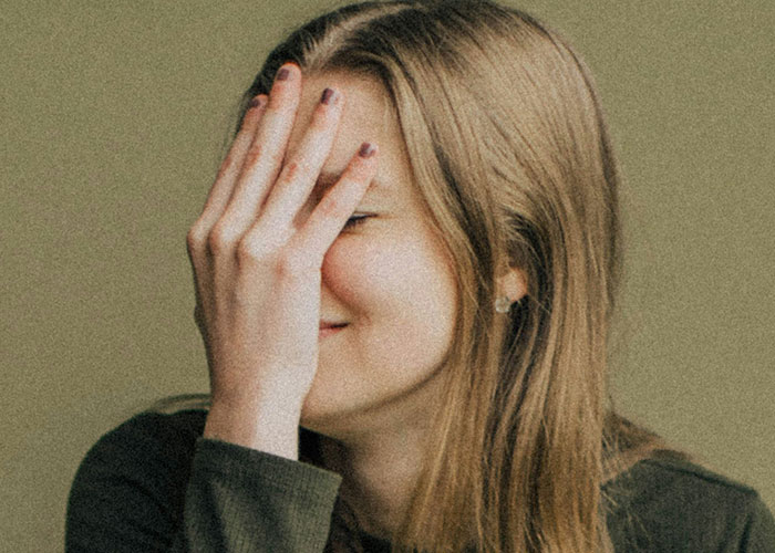 Young woman covering face with hand in a facepalm gesture, expressing frustration during a doctor’s visit experience.