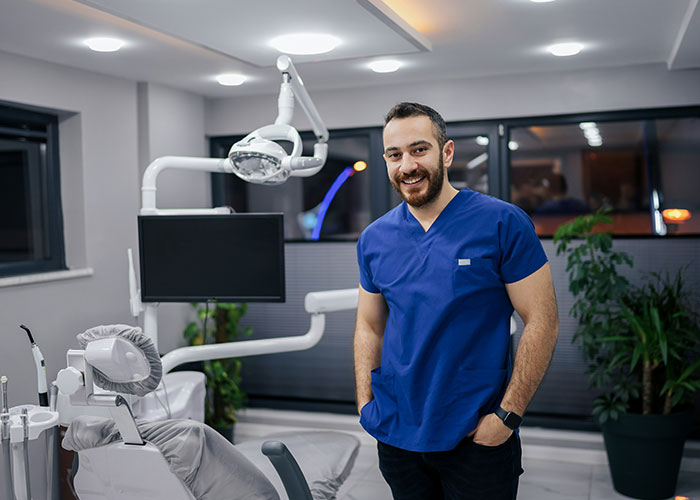 Smiling male doctor in blue scrubs standing in a modern medical office during a doctor’s appointment session.
