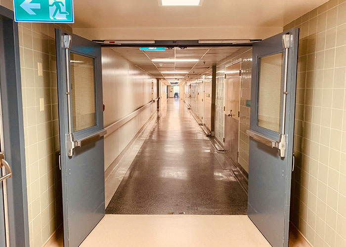 Hospital corridor with open double doors, beige walls, and a green exit sign, depicting a typical doctor’s visit setting.