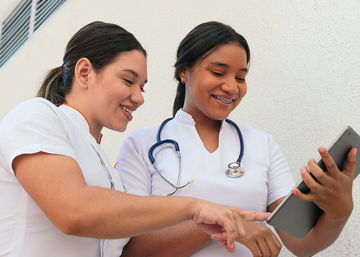 Two healthcare professionals smiling and reviewing information on a tablet during a doctor’s appointment.