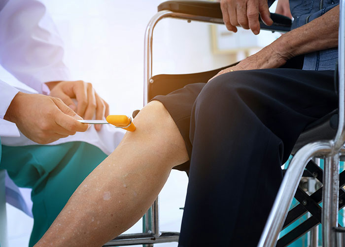 Doctor performing neurological reflex test on elderly patient's leg in a clinical setting during doctor’s appointment.
