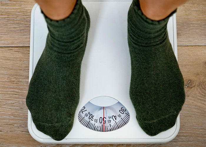 Person wearing green socks standing on a scale during a hilariously embarrassing doctor’s appointment moment.