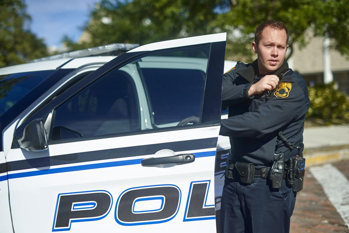 Police officer standing beside a patrol car, responding to an entitled neighbors blocked driveway complaint in a residential area.