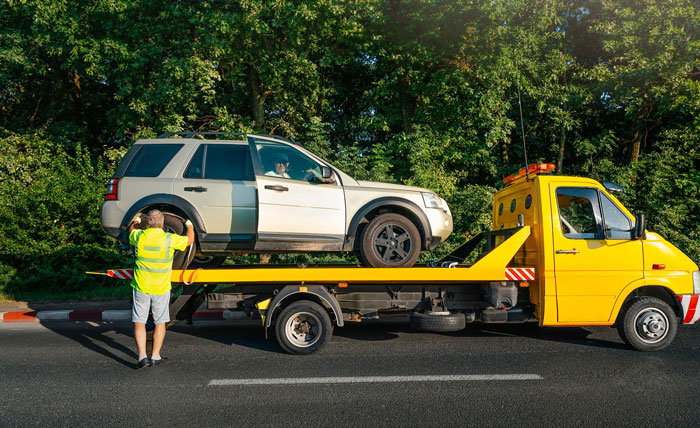Tow truck driver loading a white SUV onto a flatbed, responding to an entitled neighbors blocked driveway complaint.