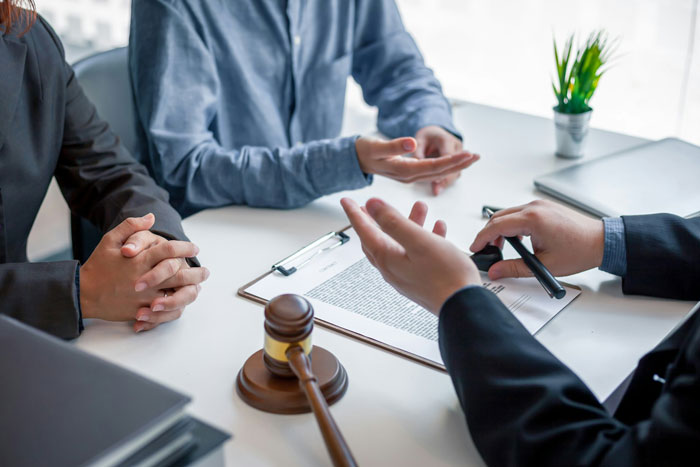 Couple consulting lawyer about adoption papers with gavel and legal documents on table in office setting.