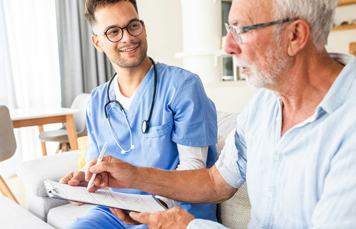 Healthcare worker in blue scrubs consulting with an elderly man, sharing critical patient care stories.
