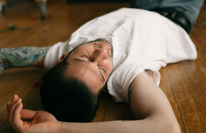 Man with tattoos lying unconscious on wooden floor, illustrating healthcare workers emergency stories.