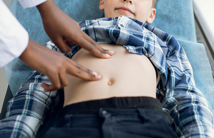 Healthcare worker examining a young boy's abdomen using fingers to check for medical issues during a clinical visit.
