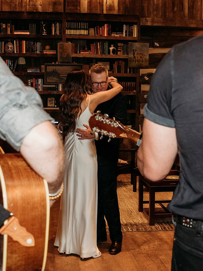 Eric Stonestreet dancing with bride at intimate wedding, musicians playing guitar in a cozy rustic setting.