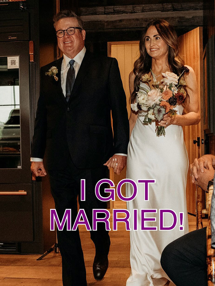 Eric Stonestreet in a suit and bride in a white dress holding flowers celebrating marriage in a cozy indoor setting
