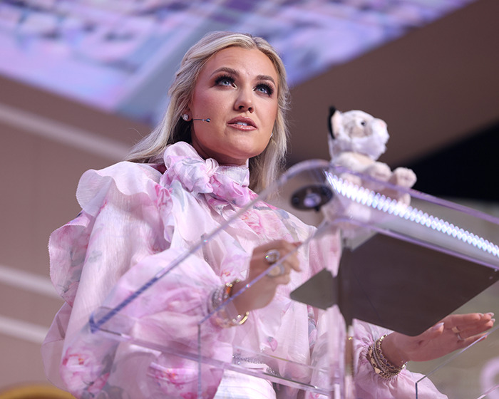 Erika Kirk speaking at a podium, highlighting her past connection to Donald Trump amid resurfacing bikini photos.