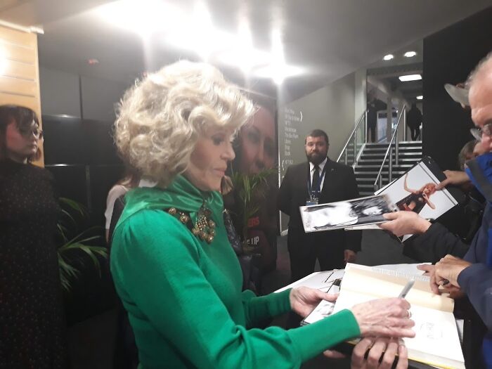 A woman in a green sweater signing autographs for fans, capturing a memorable moment meeting an idol fan experience.