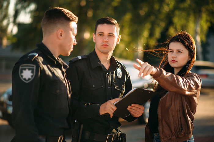 Woman points while talking to two police officers outdoors, relating to lady locks out affair partner's kid in winter.