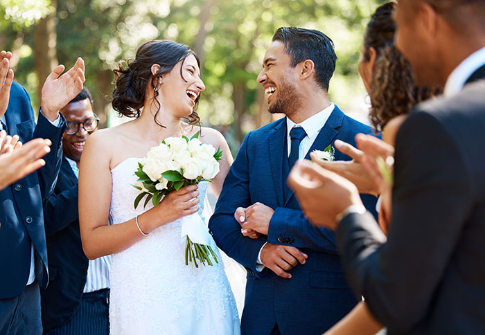 Bride and groom smiling at each other during wedding ceremony while guests applaud outdoors in daylight