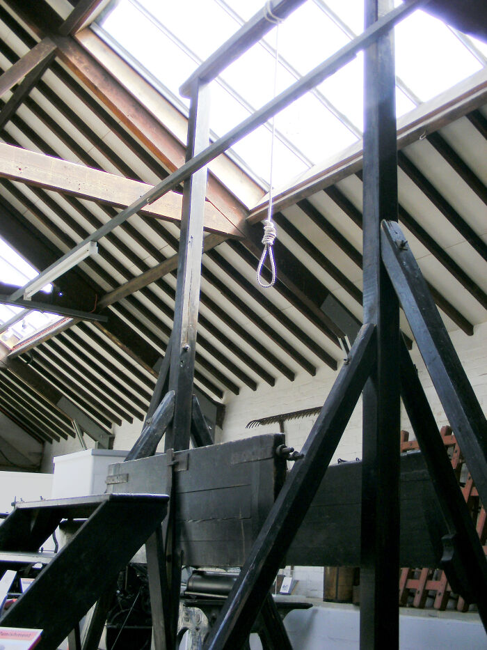 Medieval t*****e methods device featuring a large wooden guillotine under a skylight in a historic building interior.