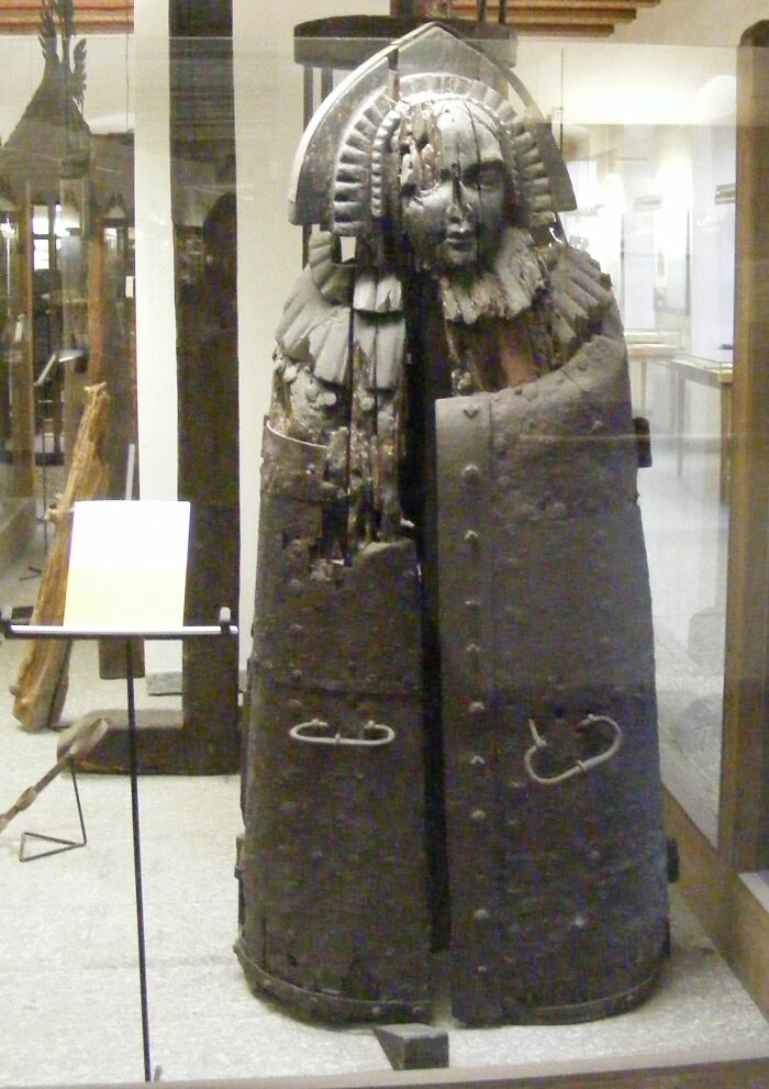 Medieval iron t*****e device shaped like a human figure with a detailed face mask and heavy metal plating.