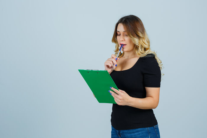 Young woman in casual clothing holding a green clipboard, thoughtfully reflecting on darkest family secrets revealed.