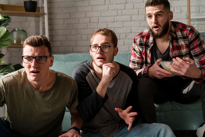 Three men sitting on a couch looking shocked and surprised, reacting to a family conflict involving a rude hubby.