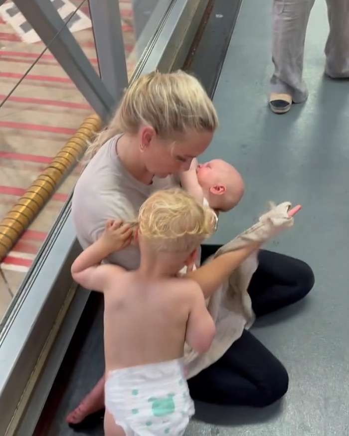 Mother comforting infant and toddler on airport floor during chaos on Paris flight trapped in dangerous heat.