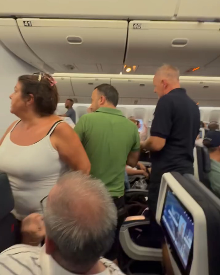 Passengers standing and looking around in an airplane cabin during chaos on Paris flight with family trapped in dangerous heat.