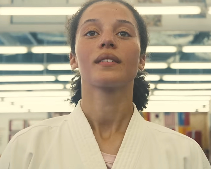 Young woman in a martial arts uniform standing confidently indoors, fans praise Chase Infiniti response to reporter question.