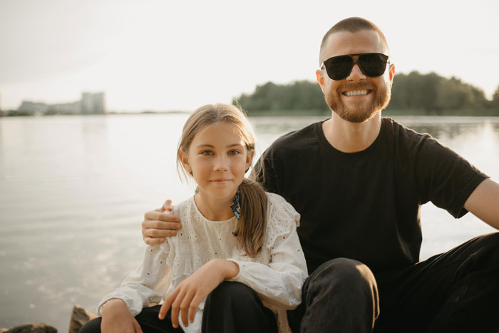 Father and 10-year-old daughter sitting by the lake, highlighting child support and parental control issues.