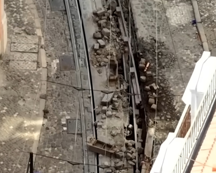 Overhead view of Lisbon crash site with damaged tram tracks and rubble after dad feared lost in Lisbon crash found alive.