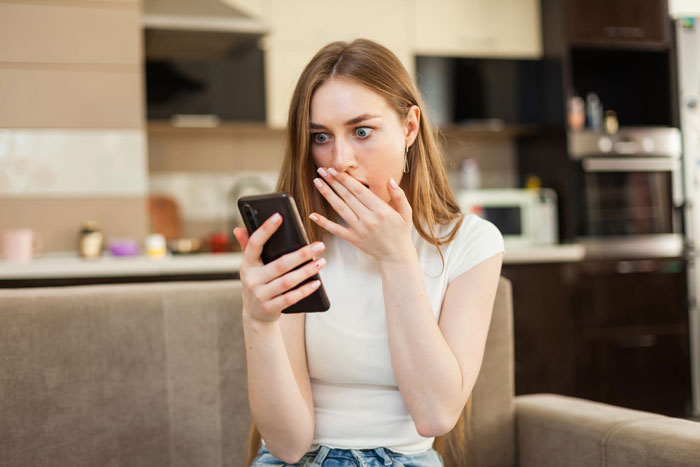 Young woman feeling sorry for friend's daughter, shocked while looking at phone in a modern kitchen setting Young woman feeling sorry for friend's daughter, shocked while looking at phone in a modern kitchen setting