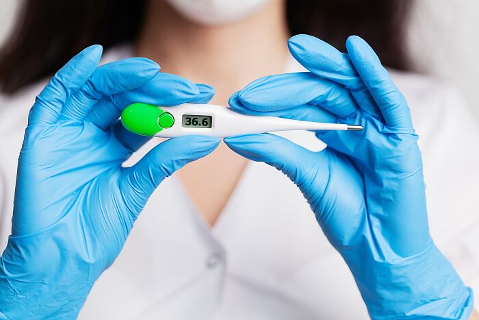 Medical professional wearing blue gloves holding a digital thermometer showing a normal reading for patients defying medical odds.