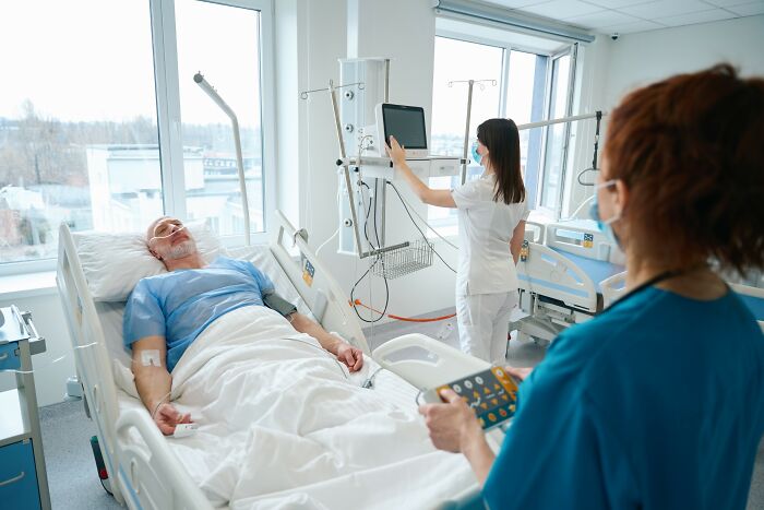 Patient defying medical odds lies in hospital bed monitored by healthcare professionals using medical equipment in a bright room.