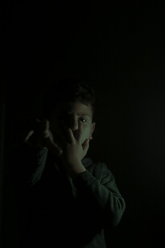 Boy alone in a dark room, looking scared and covering his mouth, capturing a frightening home alone moment.