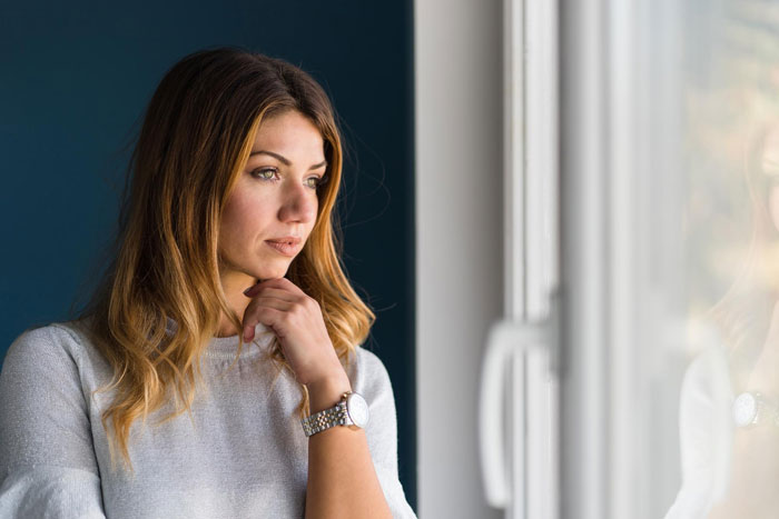 Woman looking thoughtfully out window, reflecting on fiancee’s ultimatum about 50/50 house ownership decision. Woman looking thoughtfully out window, reflecting on fiancee’s ultimatum about 50/50 house ownership decision.