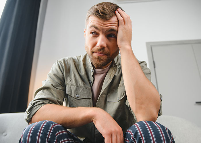 Man looking distressed and thoughtful indoors, reflecting on breakup after fiancée’s tattoo of his late brother’s face. Man looking distressed and thoughtful indoors, reflecting on breakup after fiancée’s tattoo of his late brother’s face.
