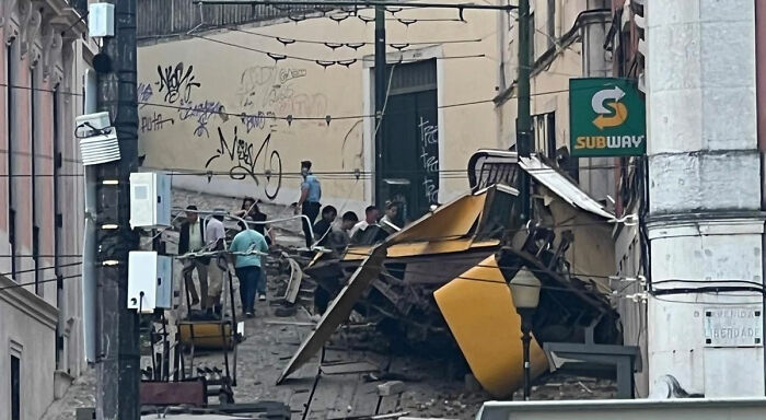 Iconic tram crashed down hill and smashed into building in Portugal with people gathered around the wreckage.
