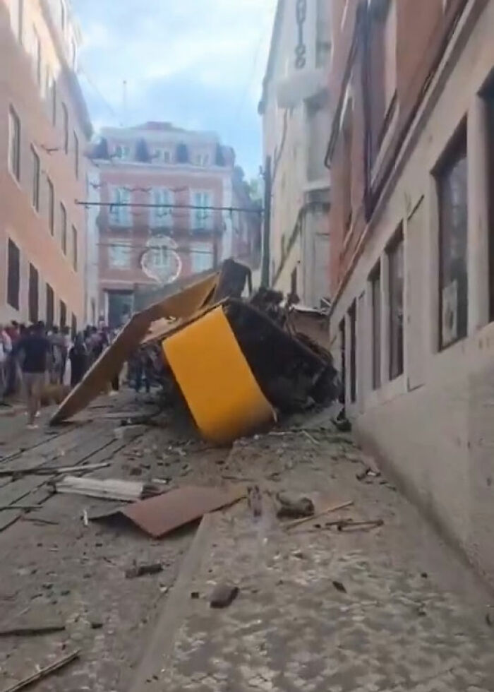 Damaged iconic tram overturned on cobblestone street after crashing into building in Portugal with debris scattered around.