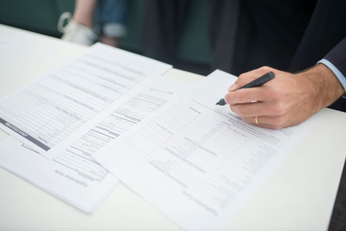 Person in business attire filling out expensive employee paperwork with a pen on a white desk surface.