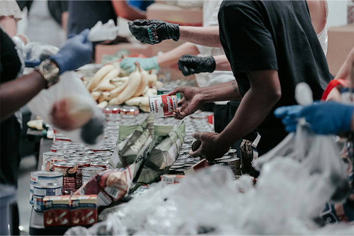 Volunteers wearing gloves distribute canned goods and food at a busy USA food bank during community outreach.