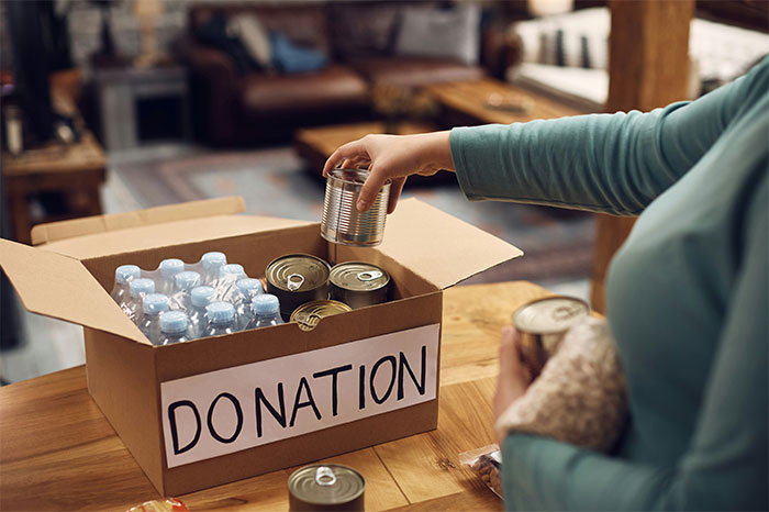 Person placing canned food in a donation box at a food bank, highlighting USA richest poor people and community aid.