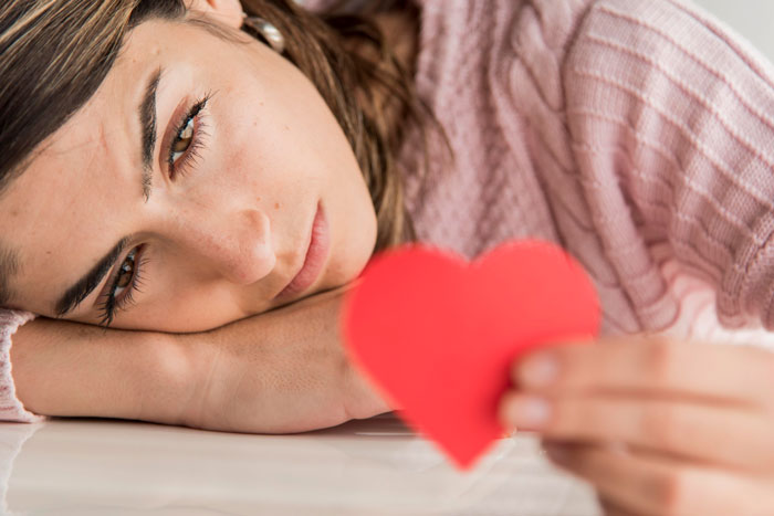 Woman lying down holding a red heart, reflecting on feelings related to found another woman Valentine card.