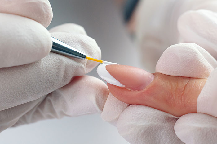 Close-up of gel nail polish application on fingernail with gloved hands using a fine brush for precision coating. Close-up of gel nail polish application on fingernail with gloved hands using a fine brush for precision coating.