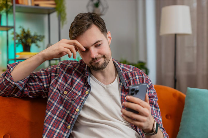 Man in plaid shirt looking at phone with concerned expression, reflecting on groom kissing best friend at bachelor party.