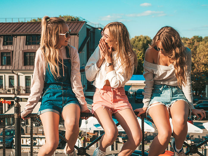 Three young women in casual summer clothes enjoying a sunny day outdoors, representing friend group plans getaway.