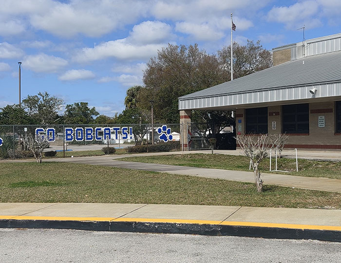 School building with Go Bobcats sign on fence under partly cloudy sky, symbolizing children turned in to police by mothers.
