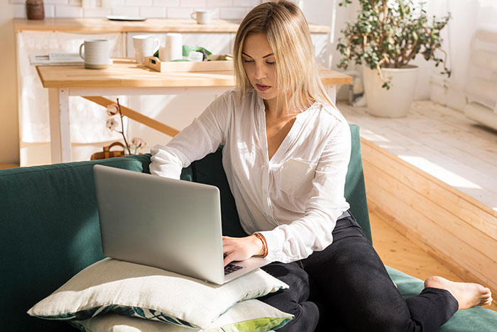 Young woman using a laptop on a couch in a bright room, reflecting on sister unwanted siblings adoption topics.