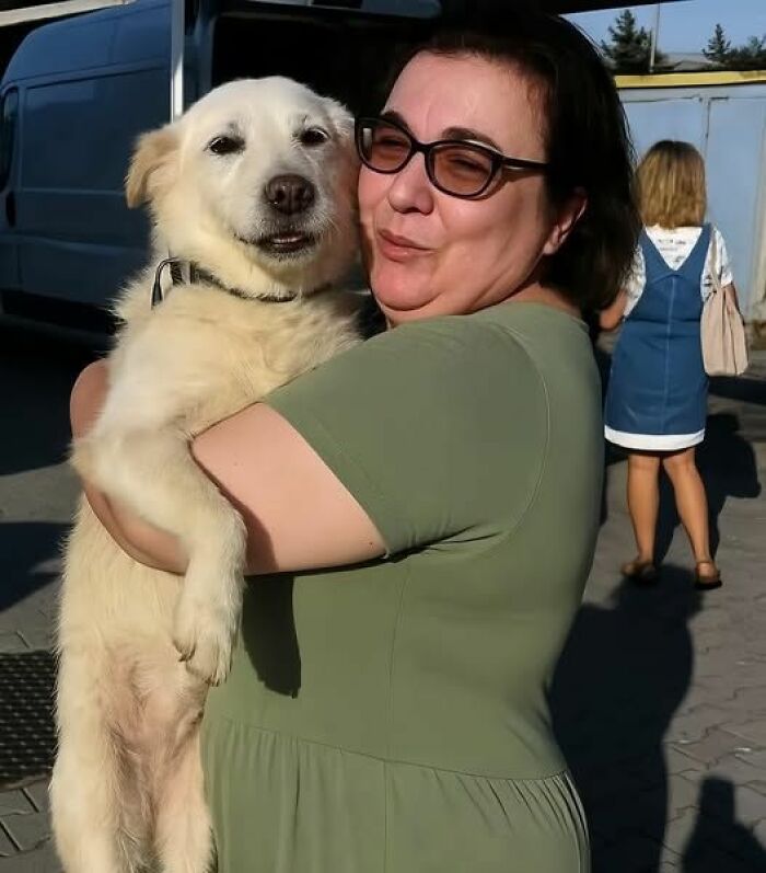 Woman wearing glasses happily holding a fluffy white dog outside, capturing a moment of fun with animals and joy.