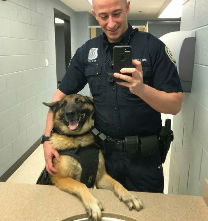 Police officer taking a selfie with a happy K9 dog, showcasing fun with animals in a wholesome moment.