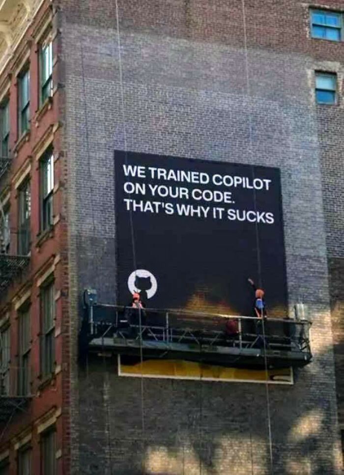 Large black banner on a brick wall with a funny programming meme about Copilot, featuring workers installing the sign outside.